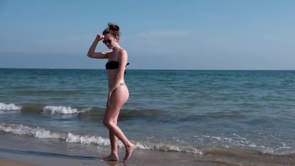 穿着比基尼的年轻性感女孩的慢动作 一个美丽的身影摆姿势 在阳光明媚的夏日沿着海滩散步 — 图库视频影像