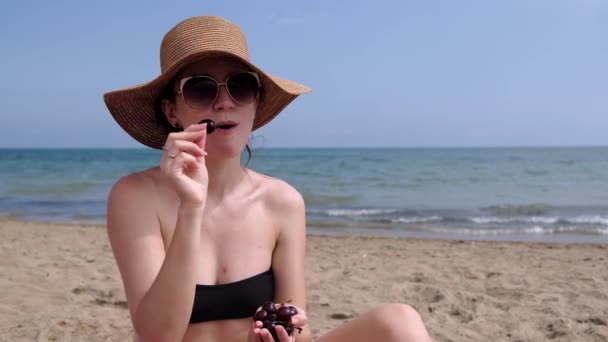 Mladá Žena Nosí Bikiny Slaměný Klobouk Jíst Třešně Pláži Moře — Stock video