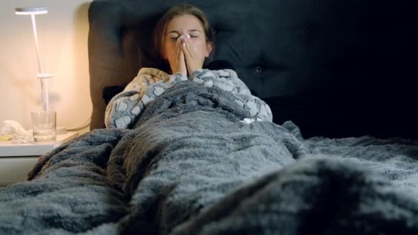 ベッドの彼女の鼻を吹くと組織をスローで発熱を伴う若いうんざりしている女性 温度計 ガラス テーブルの上の水の — ストック動画