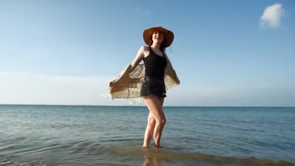 Молодая женщина в соломенной шляпе наслаждается и танцует у моря — стоковое видео