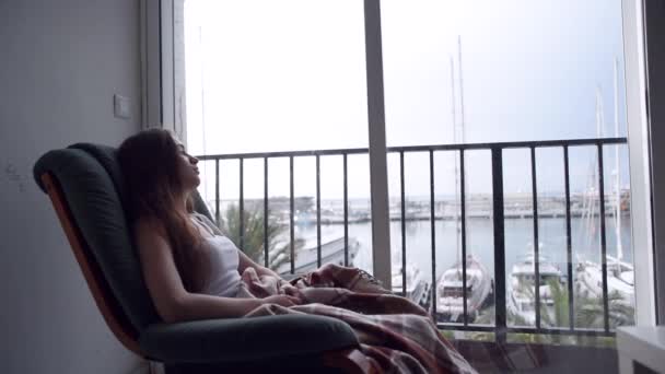 ヤングは落ち込んで椅子のスイングと海に窓の外見ている女性です 外は雨 絶望の中で孤独な女性 — ストック動画