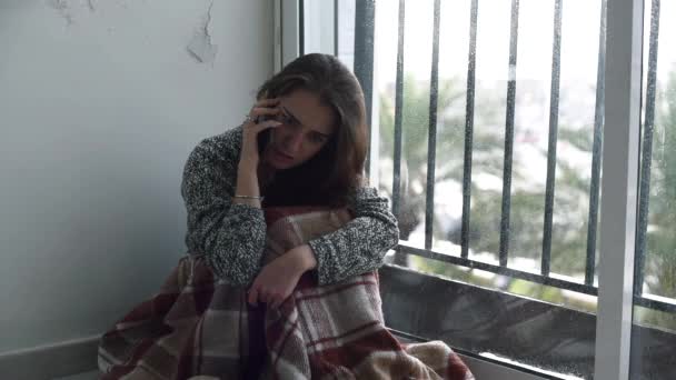 落ち込んだ女性が携帯電話で話している叫んでいるとそとは雨で窓際の床に座って泣いています 自殺の考えと絶望の中で孤独な女性 — ストック動画