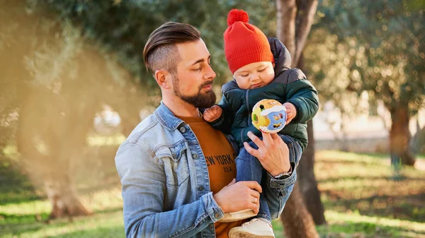 一个留胡子的年轻男子在公园散步和玩耍时 手里拿着他可爱的小儿子的肖像 父亲和儿子 — 图库照片