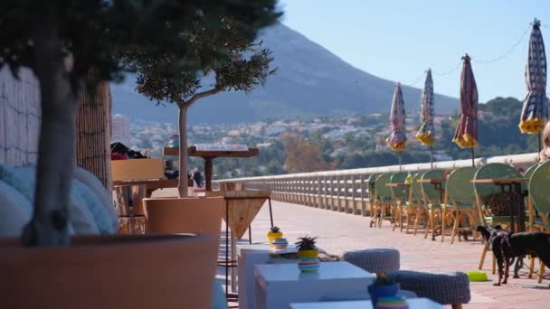 スペインの町デニアの Montgo 山の美しい景色と居心地の良いビーチ カフェ 木製のテーブルと椅子の海の海岸によって クライアントの準備 — ストック動画