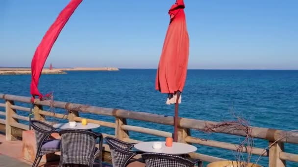 海の上の美しい景色とスタイリッシュなビーチのカフェ 木製のテーブルと椅子の海の海岸によって クライアントの準備します 色鮮やかな旗が風に手を振る — ストック動画