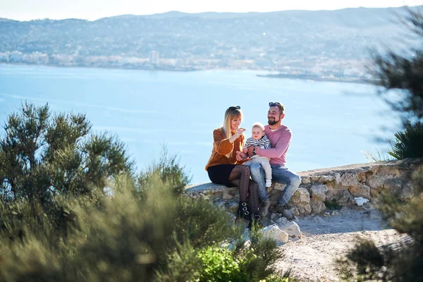 Glückliche junge Familie mit kleinem netten Jungen genießt den sonnigen Tag am Meer — Stockfoto