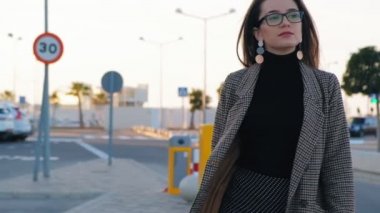 Otoparkta yürüyen gözlüklü genç kendine güvenen iş kadınının yavaş hareketi. Güneşli bir günde yürüyen şık kadın.