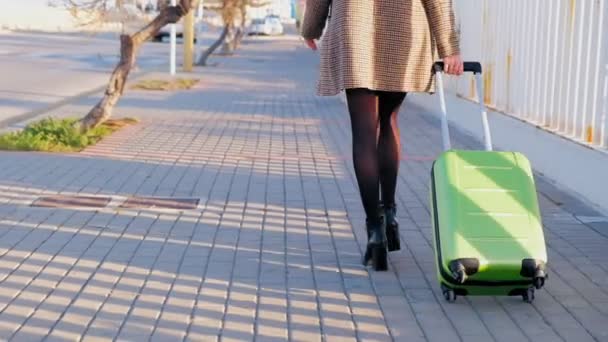 緑のスーツケースを持って歩くハイヒールの若いビジネスウーマンのバックビュー 彼女のフライトに急いでスーツケースを持つスタイリッシュな女性 スローモーション — ストック動画