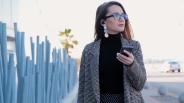 Elinde yeşil bavul ve cep telefonu ile yürüyen gözlük genç başarılı iş kadını yavaş hareket. Kulakta bavul ve bluetooth ile şık kadın.