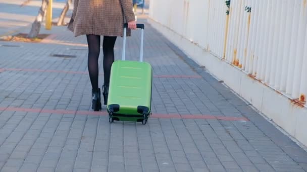 緑のスーツケースを持って歩くハイヒールの若いビジネスウーマンのバックビュー 彼女のフライトに急いでスーツケースを持つスタイリッシュな女性 スローモーション — ストック動画