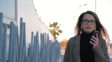 Elinde cep telefonu ile yürüyen gözlükgenç başarılı iş kadını yavaş hareket. Şık başarılı kadın telefonda konuşuyor.
