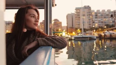 Bir deniz teknesinde gün batımının tadını çıkaran genç ve çekici bir kadının portresi. Arka planda binalar ve şehir ışıkları. Denia, İspanya.