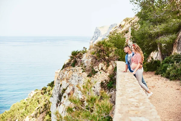 Young pregnant woman posing with her husband with sea on background — Stock Photo, Image