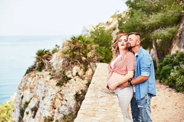 Giovane donna incinta in posa con il marito con il mare sullo sfondo — Foto Stock