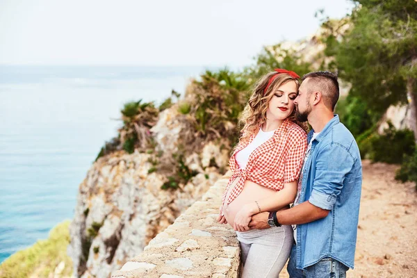 Giovane donna incinta in posa con il marito con il mare sullo sfondo — Foto Stock