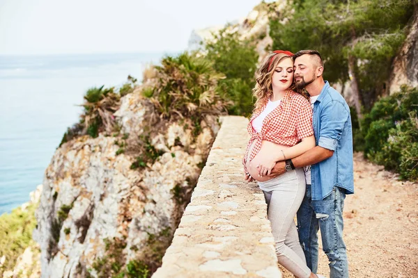 Giovane donna incinta in posa con il marito con il mare sullo sfondo — Foto Stock