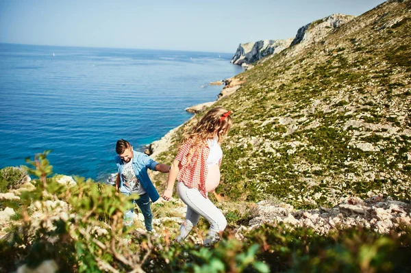 Junge schwangere Frau läuft mit ihrem Mann vor dem Hintergrund des Meeres — Stockfoto