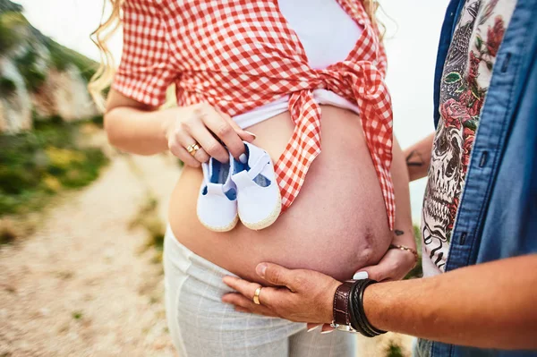 Close-up of pregnant woman and men holding a tiny shoes on belly. — Stock Photo, Image