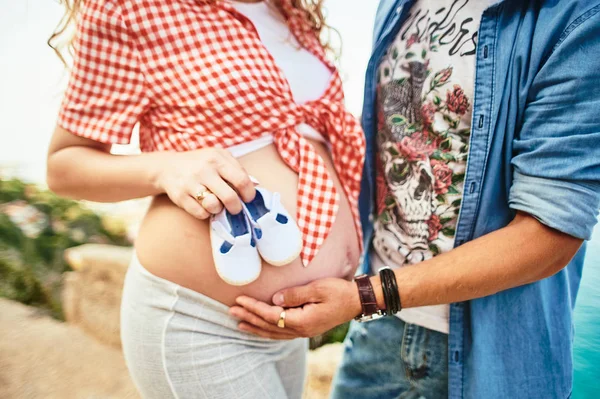 Close-up of pregnant woman and men holding a tiny shoes on belly. — Stock Photo, Image