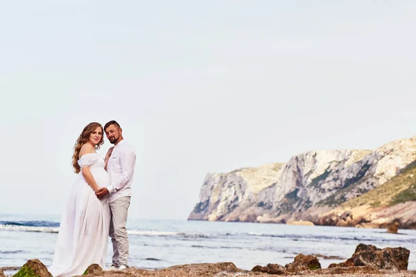 Young pregnant woman posing with her husband on the beach — 스톡 사진