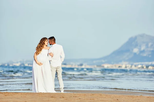 Молода вагітна жінка позує зі своїм чоловіком на пляжі — стокове фото