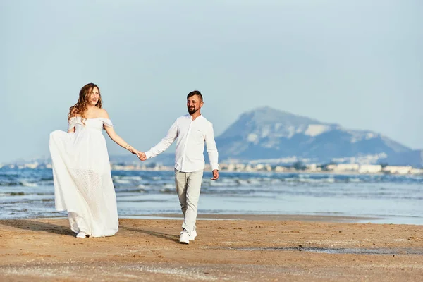 Młoda ciężarna kobieta spacerująca z mężem po plaży — Zdjęcie stockowe