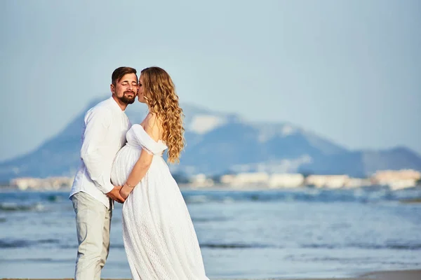Piękna kobieta w ciąży całuje się z mężem na plaży — Zdjęcie stockowe