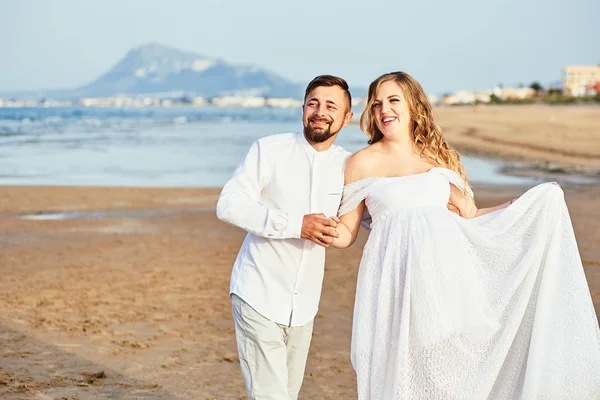 Молодая беременная женщина позирует со своим мужем на пляже — стоковое фото