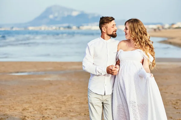 Giovane donna incinta in posa con il marito sulla spiaggia — Foto Stock