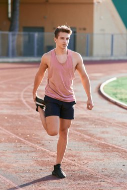 Young man runner stretching his leg on race track in stadium
