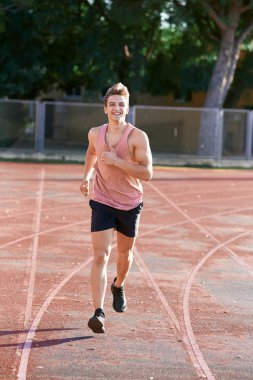 Genç kaslı adam pistte koşuyor.