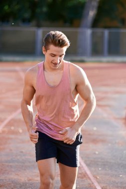Genç kaslı adam pistte koşuyor.