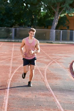 Genç kaslı adam pistte koşuyor.
