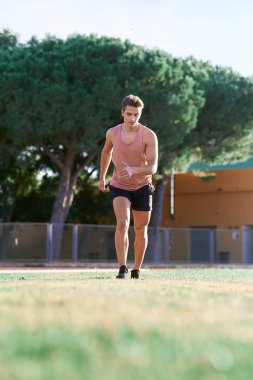 Genç kaslı adam pistte koşuyor.