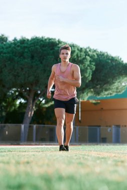 Genç kaslı adam pistte koşuyor.