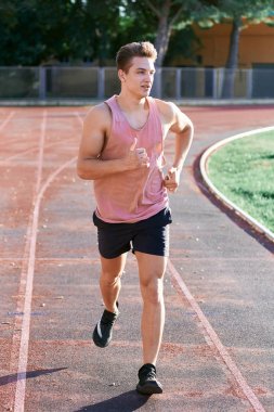 Genç kaslı adam pistte koşuyor.