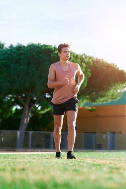 Genç kaslı adam pistte koşuyor.