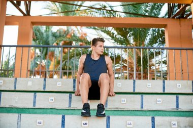 Genç kaslı adam stadyumda ters şınav çekiyor.