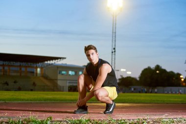 Young man runner tying shoelaces on stadium.