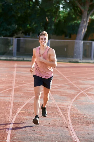 Genç kaslı adam pistte koşuyor.