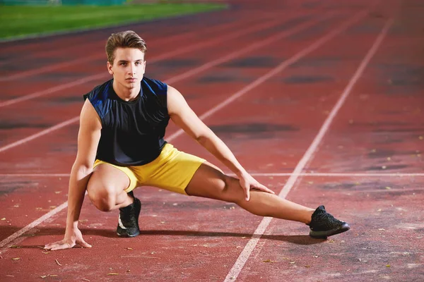 Young man runner stretching his leg on race track in stadium