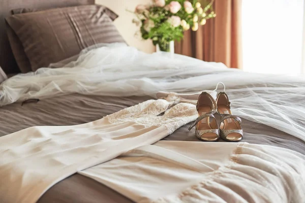 Biała elegancka suknia ślubna i buty leżące na łóżku. — Zdjęcie stockowe