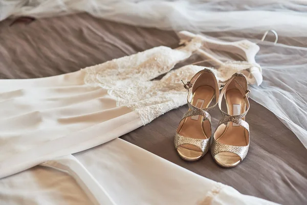 Robe de mariée élégante blanche et chaussures couchées sur le lit . — Photo