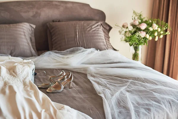 Vit elegant bröllopsklänning, slöja och skor liggande på sängen. — Stockfoto