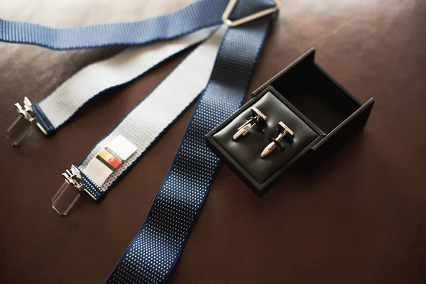 Top view of men\'s accessories on a dark background: suspenders and cufflinks.