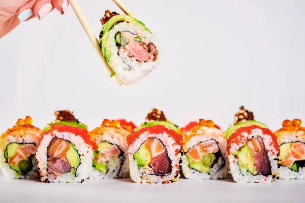 Primer plano de los rollos de sushi uramaki y rollo de mano femenina con palillos — Foto de Stock