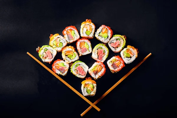 Top view of sushi and rolls pieces placed between chopsticks on black background — Stock Photo, Image