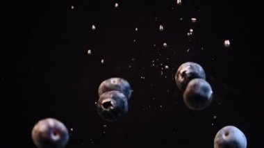 Siyah arka plan karşı kabarcıklar ile suya düşen yaban mersini yavaş hareket. Taze meyveler bir kapta batıyor. Makro.