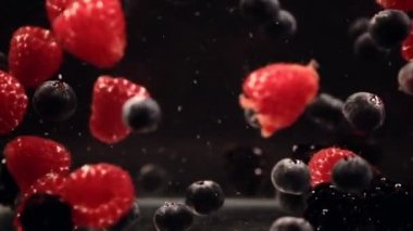 Siyah arka plan karşı suda yüzen yaban mersini ve ahududu yavaş hareket. Taze meyveler bir kapta batıyor. Kopyalama alanı.