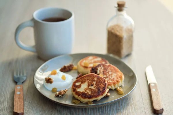 Close-up of homemade cheese pancakes syrniki with sour cream and cup of tea — Stock Photo, Image